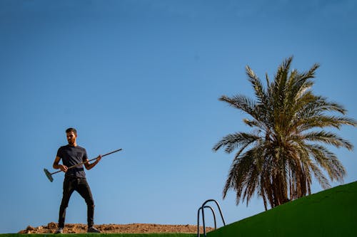 Trendy man with broom imitating guitar playing near palm tree