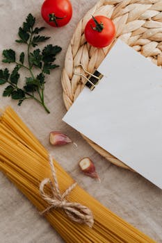 Top view of Italian cooking ingredients with spaghetti, tomatoes, garlic, and blank menu paper.