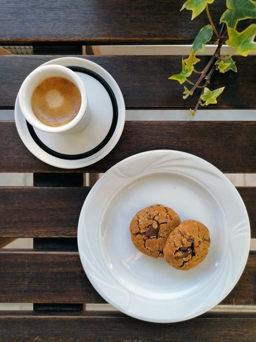 Free A cozy scene with a cup of coffee and chocolate chip cookies on a wooden table. Stock Photo