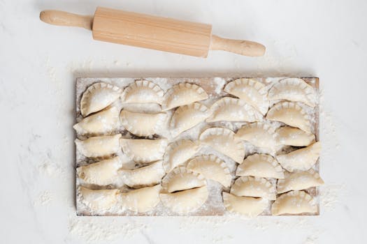 Top view of homemade pierogi arranged on a floured wooden board with a rolling pin.