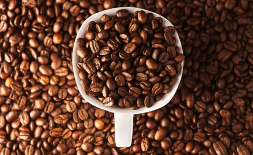 Free Close-up photo of roasted coffee beans in a mug surrounded by more beans. Ideal for coffee lovers. Stock Photo