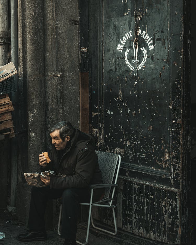 Man In Black Jacket Sitting On Chair Eating