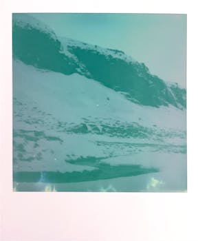 Vintage polaroid capturing a snowy mountain landscape with a teal tint.