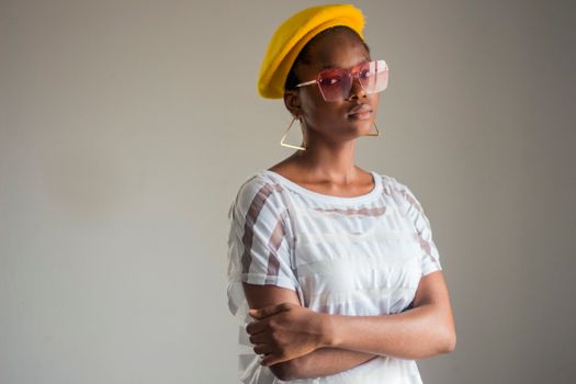 Stylish portrait of a confident African woman wearing a yellow beret and sunglasses, posing indoors.