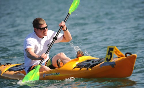 Free Smiling Man in White Crew Neck T Shirt Wearing Sunglasses Paddling on Yellow Kayak during Daytime Stock Photo