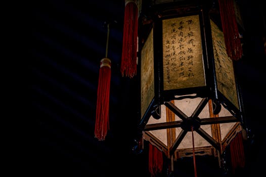 From below of aged symmetric decorative lantern made of wooden beams in oriental style hanging near red threads in cafe at night