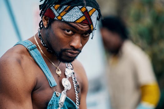 Serious man in denim overalls with bandana, focusing outdoors. Modern style.