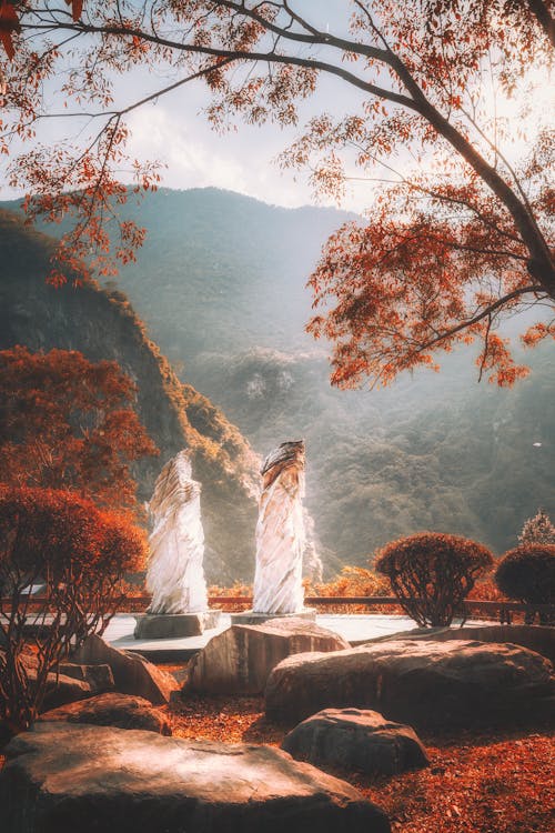 Old creative statues near mountains and bright autumn trees