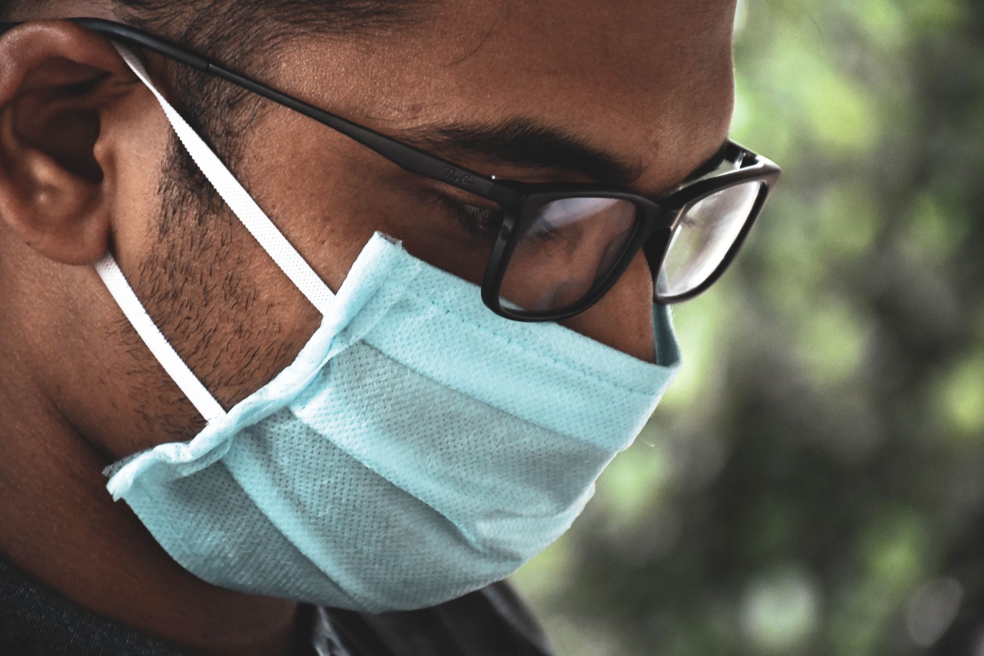A man wearing eyeglasses and a surgical mask outdoors, focusing on health safety.