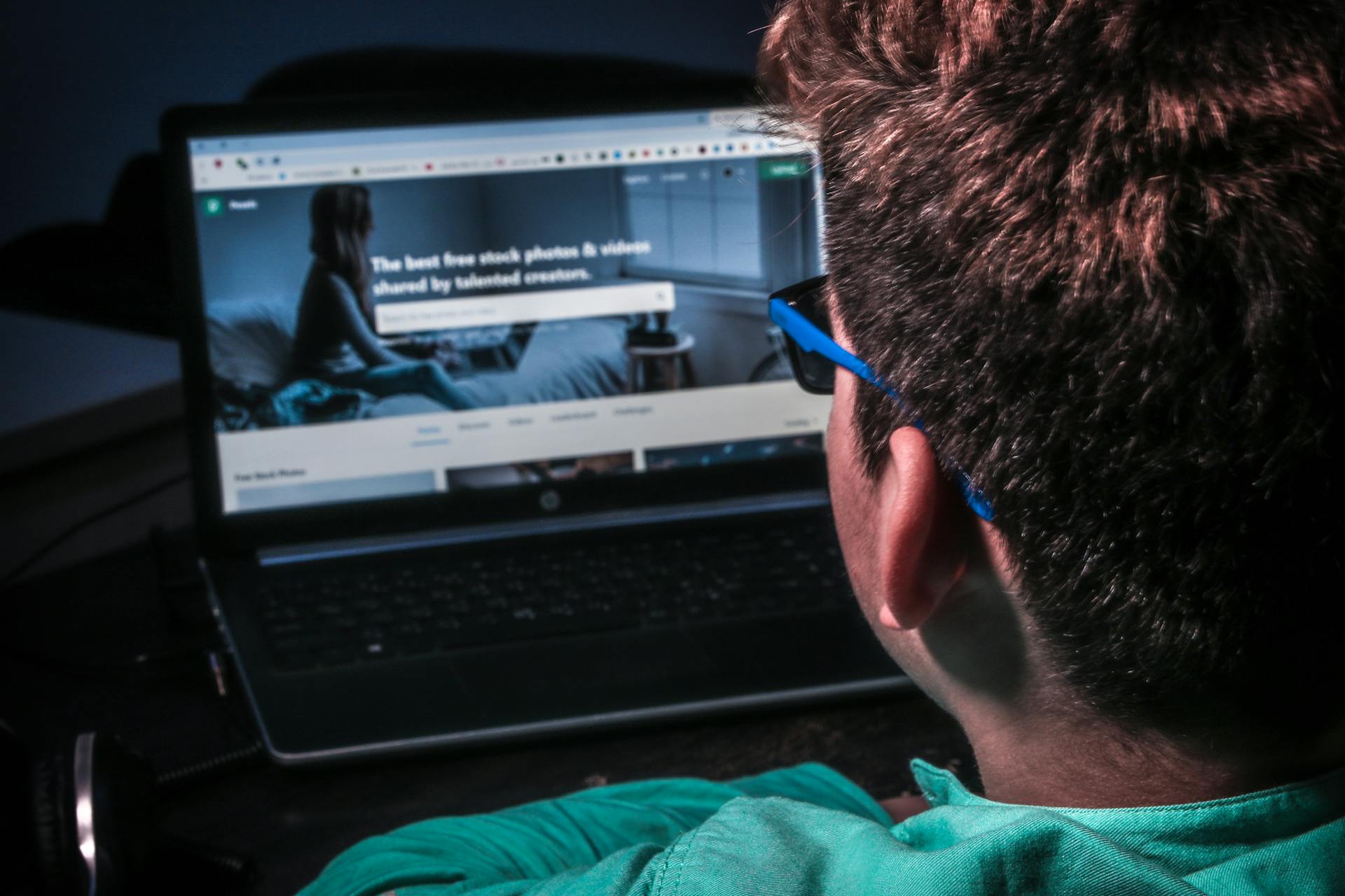 A Man in Teal Shirt in Front of a Laptop with the Pexels Page on Screen