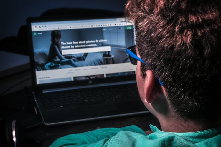 A Man In Teal Shirt In Front Of A Laptop With The Pexels Page On Screen