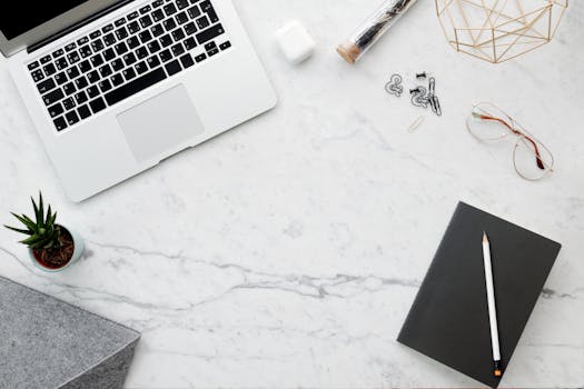 Flat lay of a modern workspace with a laptop, notebook, and office accessories on a marble surface.