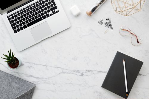 Free Flat lay of a modern workspace with a laptop, notebook, and office accessories on a marble surface. Stock Photo