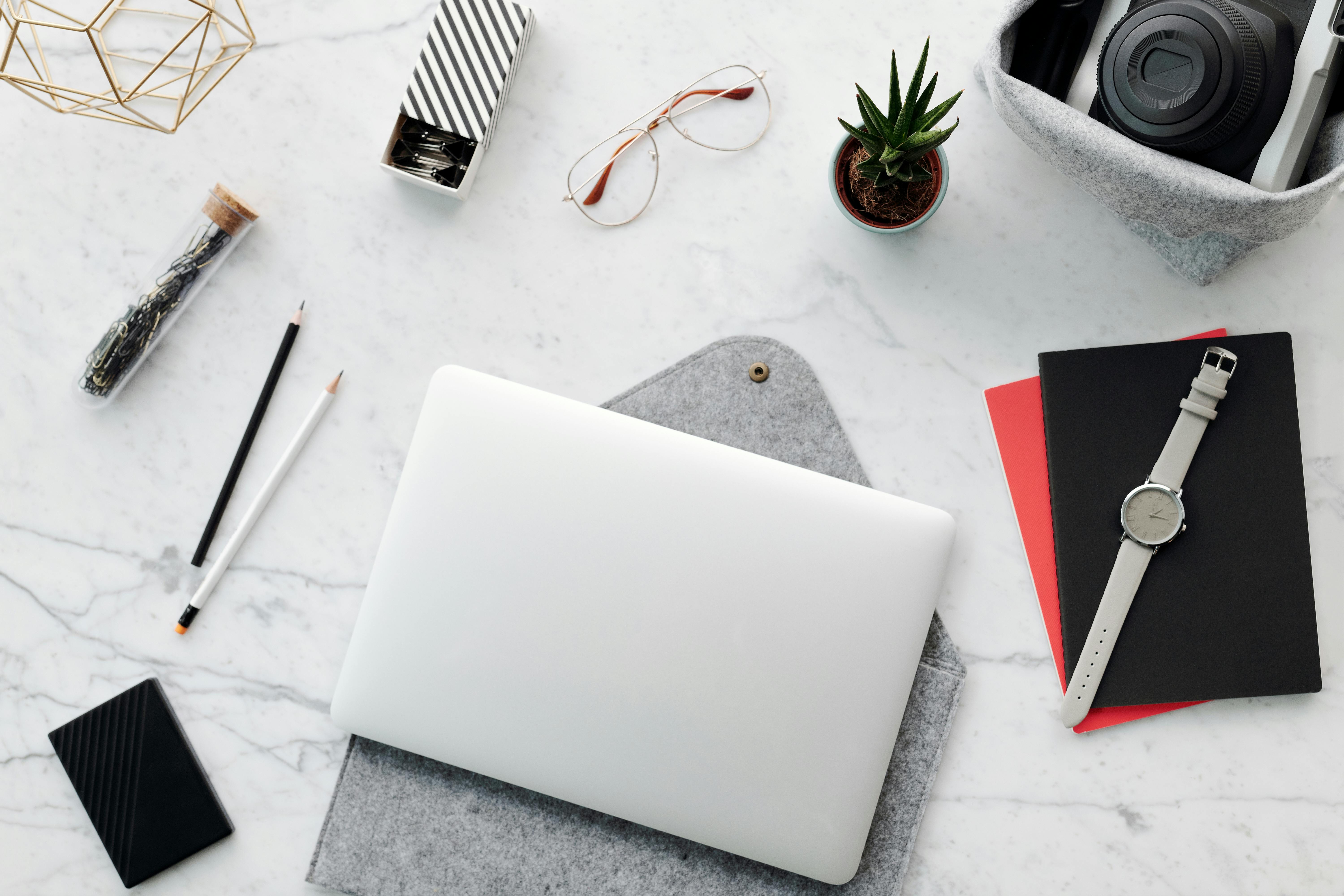 A stylish workspace featuring a laptop, camera, plants, and office supplies on a marble table.