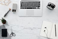 时尚工作空间采用平坦布局，大理石桌面上摆放着笔记本电脑、工厂模型和文具