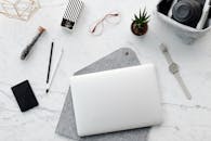 一张极简主义工作空间的顶视图，大理石桌面上摆放着笔记本电脑、相机和办公配件