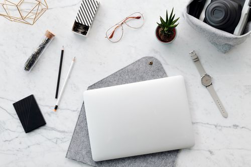 Free Top view of a minimalist workspace featuring a laptop, camera, and office accessories on a marble surface. Stock Photo