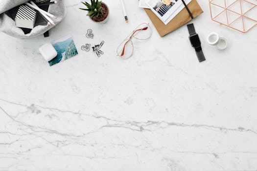 Top view of an organized workspace with eyeglasses, smartwatch, and stationery on marble.