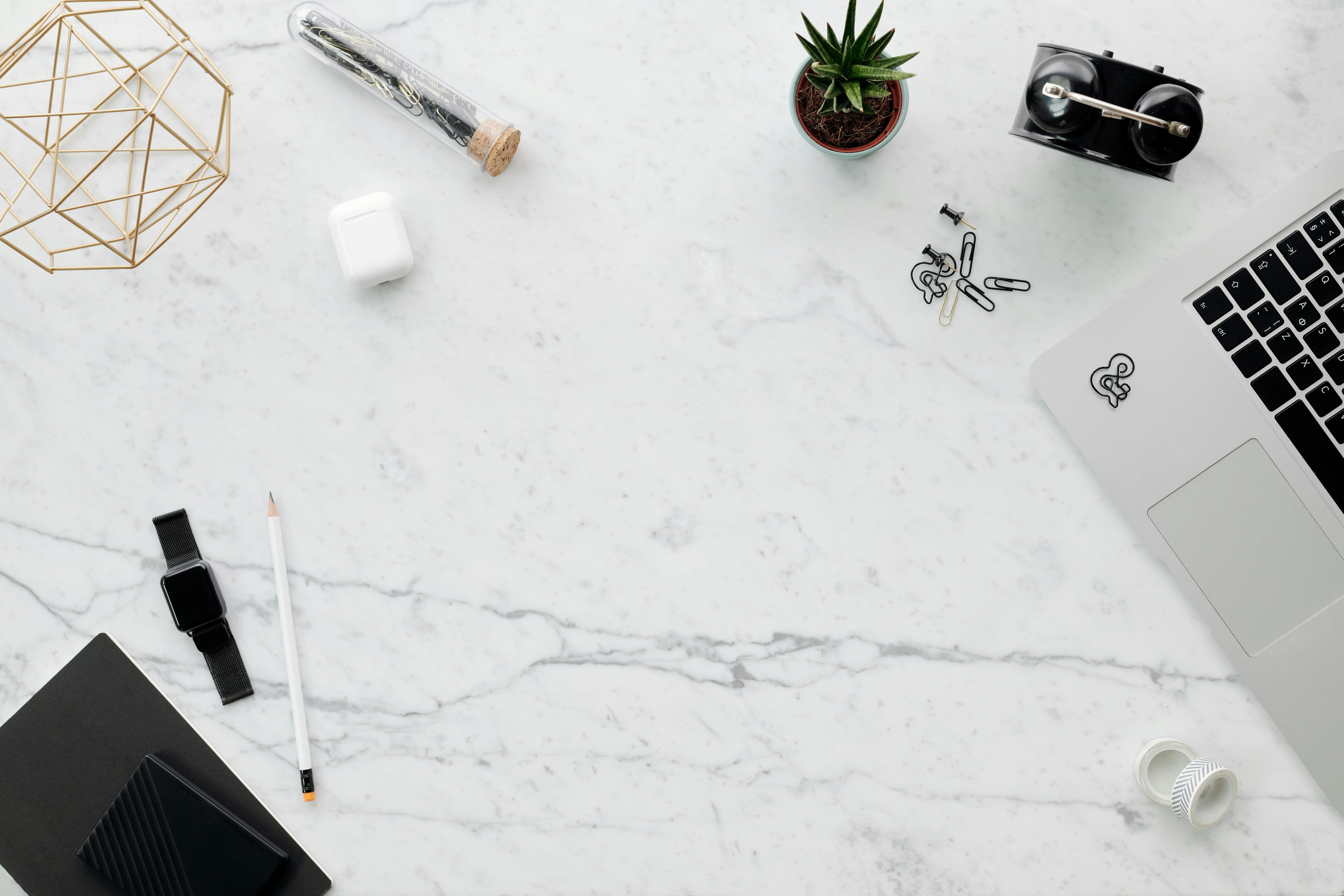 Top view of a minimalist home office setup on a marble desk featuring gadgets and stationery items.