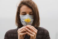 一位戴着口罩的女人手持一朵黄花，象征着保护与希望