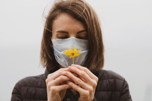 一位戴着口罩的女人手持一朵黄花，象征着保护与希望