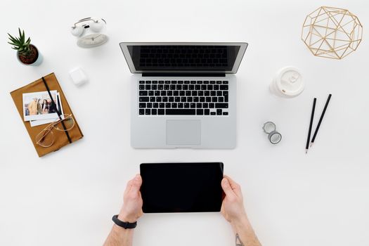 Flat lay of a modern workspace with laptop, tablet, and stationary on a white desk.