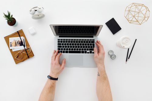 Free Top view of a minimalist workspace featuring a laptop, office supplies, and a person's hands typing on a laptop. Stock Photo
