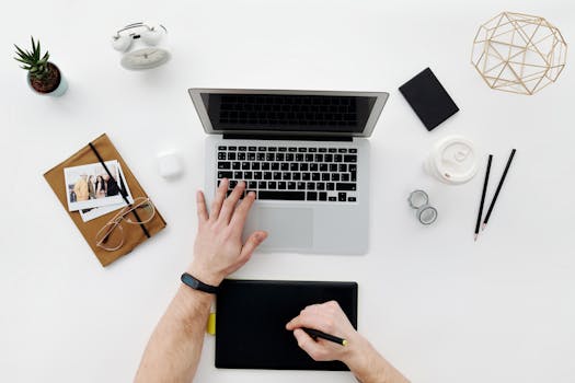 Modern workspace featuring a laptop, drawing tablet, and office essentials from above.