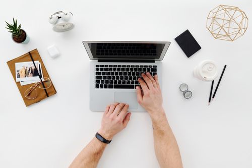 Free Top view of a minimalist desk layout with a laptop, office supplies, and a person's hands in use. Stock Photo