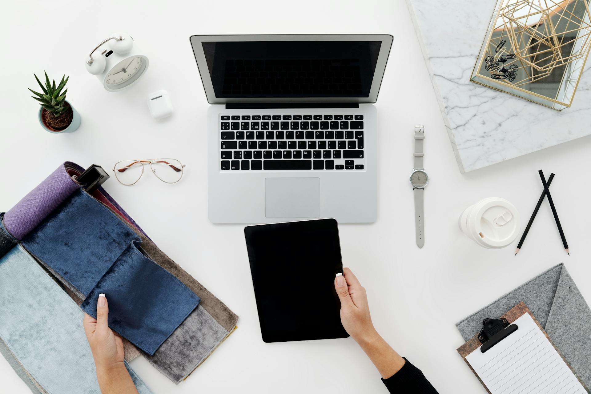 Creative workspace setup with laptop, tablet, and designer tools on a white table.