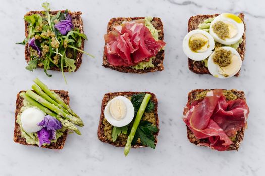 Top view of six gourmet sandwiches featuring artisanal ingredients like avocado, asparagus, and cured meats.