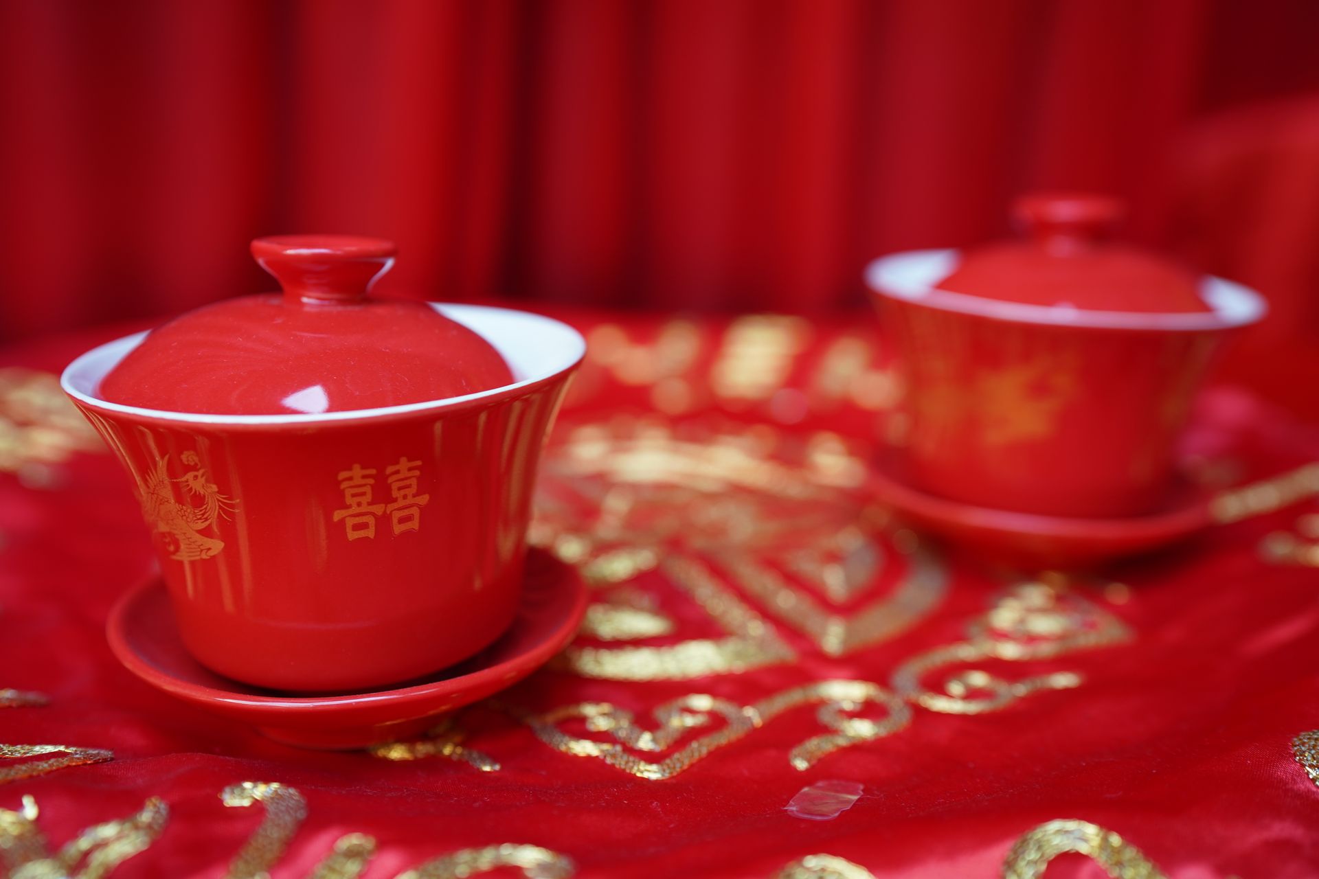 Elegant red Chinese tea cups with traditional symbols on a decorative tablecloth.