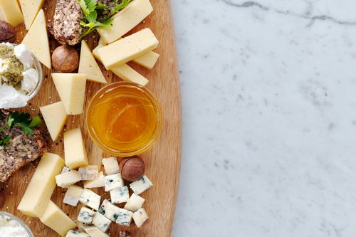 Free Top view of a gourmet cheese board with assorted cheeses, honey, and nuts on a wooden board over marble surface. Stock Photo