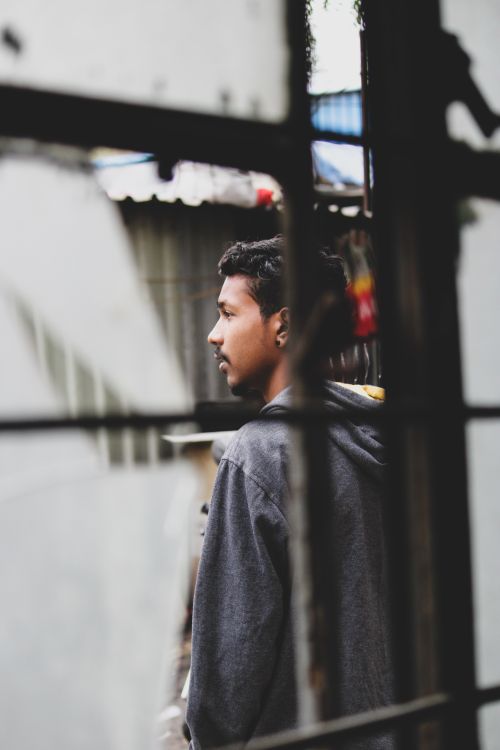 Free Side view of young ethnic guy in casual clothes standing outside window with broken glass and looking away pensively on street on daytime Stock Photo
