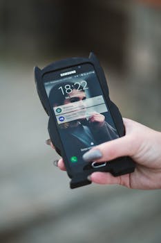 Close-up of a hand holding a smartphone displaying notifications outdoors.