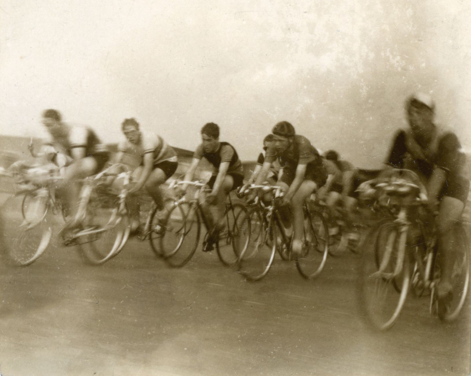 A vintage photograph of cyclists racing, captured in sepia tone, showcasing a classic cycling event.