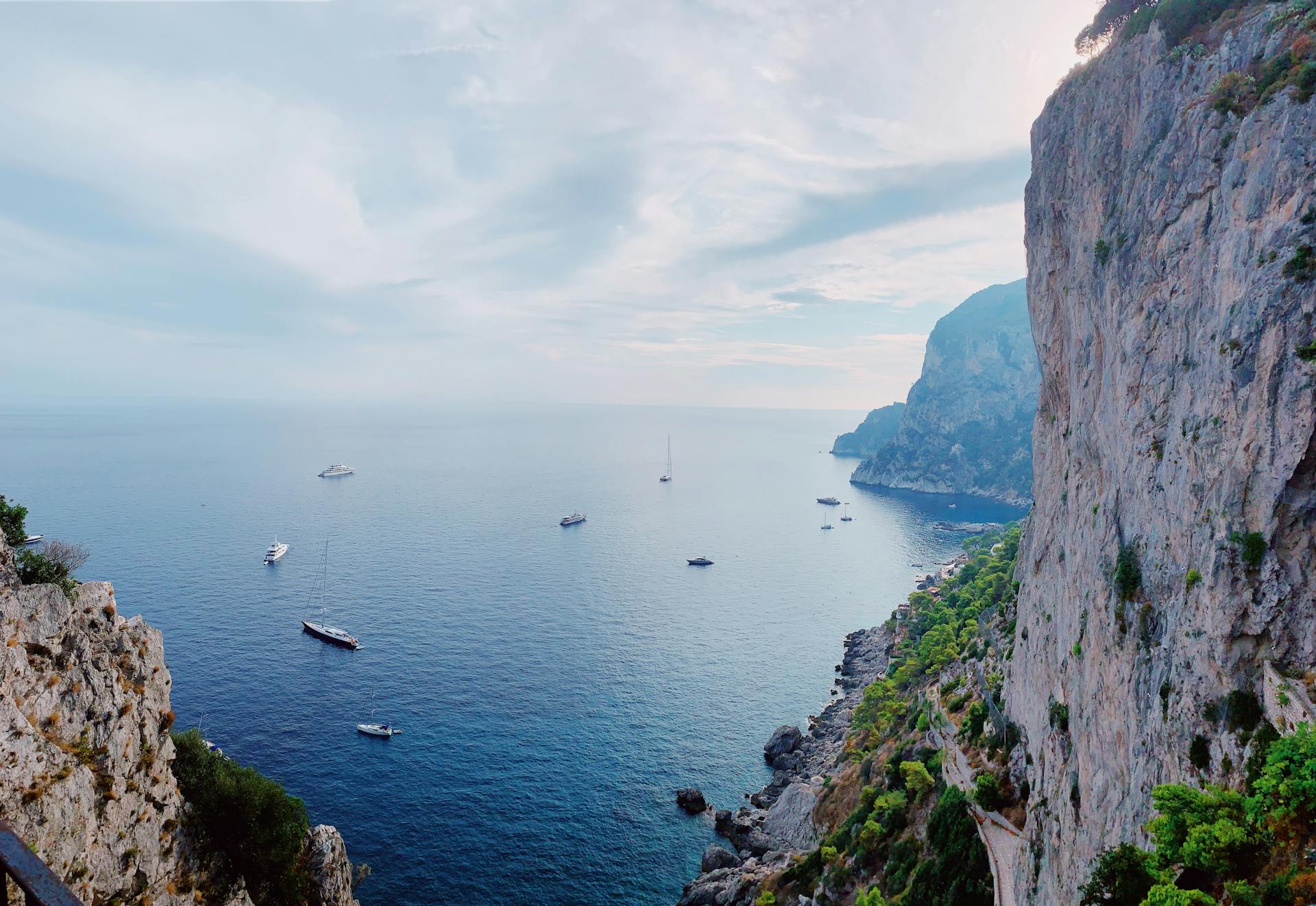 Breathtaking view of Capri cliffs and sailboats on a clear day in Italy.