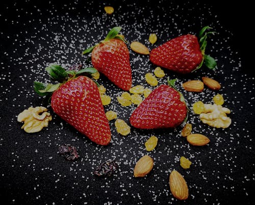 From above of ripe delicious sweet strawberries and raisins served on black plate with scattered healthy almonds and walnuts decorated with white seeds