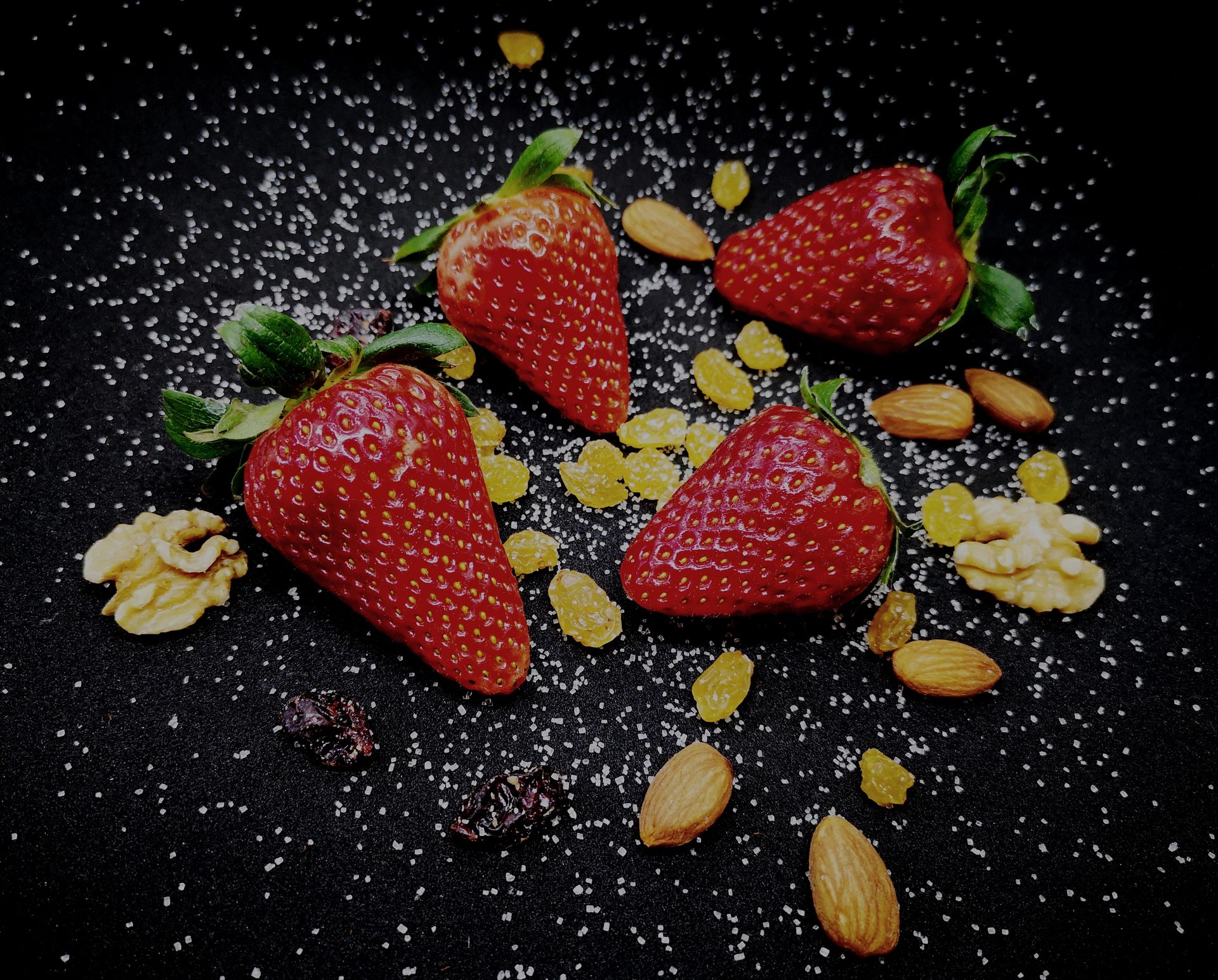 From above of ripe delicious sweet strawberries and raisins served on black plate with scattered healthy almonds and walnuts decorated with white seeds
