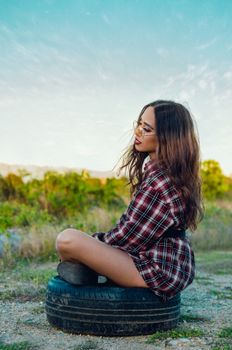 一位穿着格子衬衫的年轻女子坐在户外的轮胎上，享受着大自然