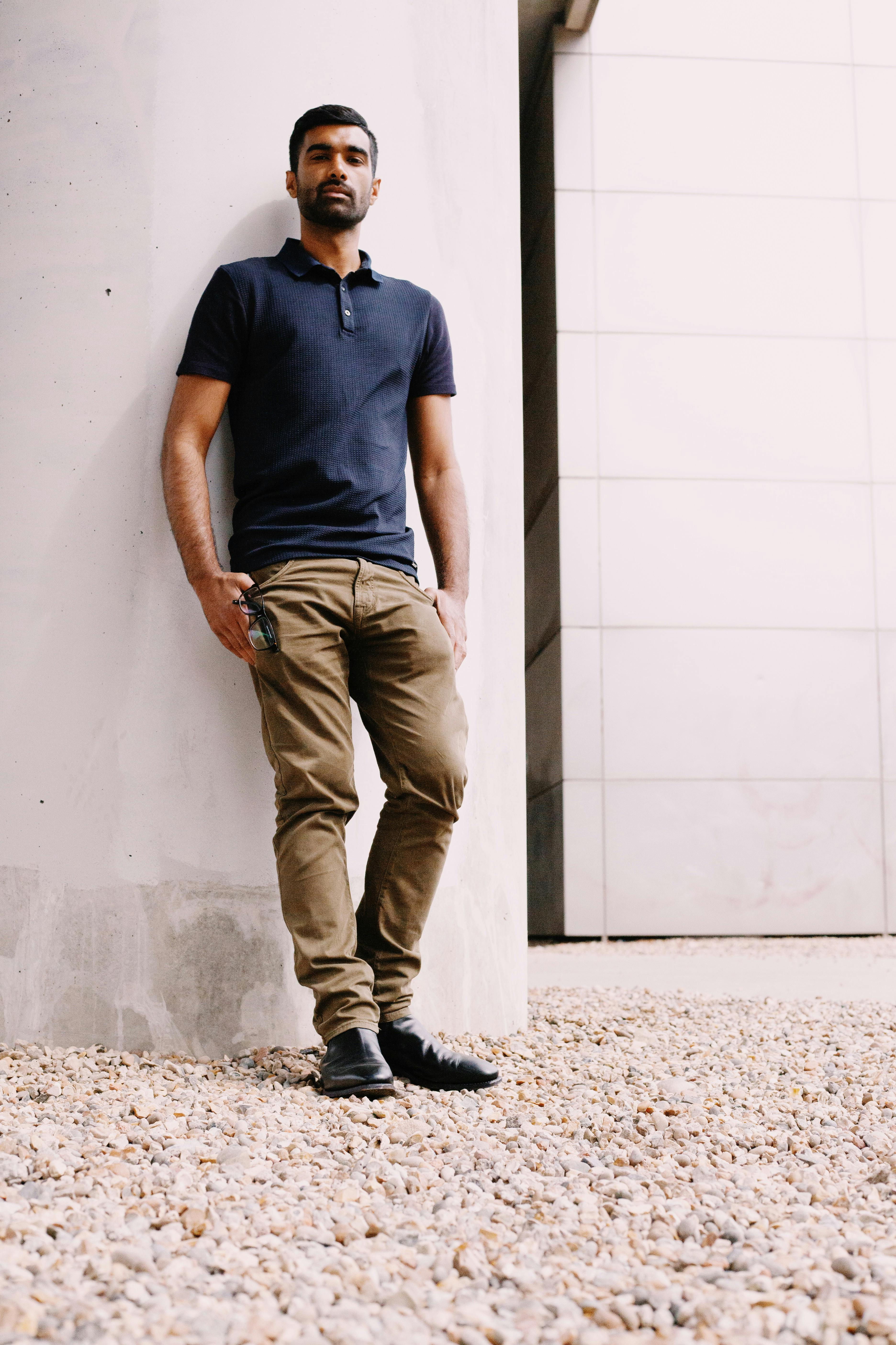 Man In Blue Crew Neck T Shirt And Brown Pants Leaning On White