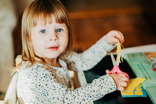 Young girl using scissors for arts and crafts in a cozy indoor setting.