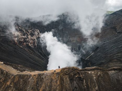Drone view of anonymous traveler enjoying amazing view of volcano crater during trip in highland