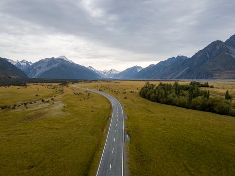 Aerial view of an empty road winding through Mount Cook National Park in New Zealand, flanked by majestic mountains.