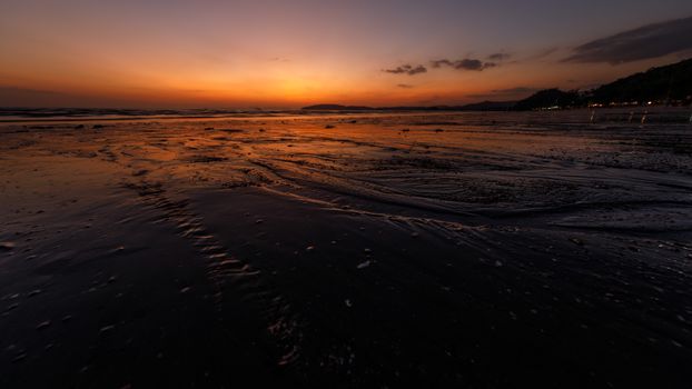 Serene sunset view over a tranquil beach in Krabi, Thailand with warm orange hues reflecting on the shore.