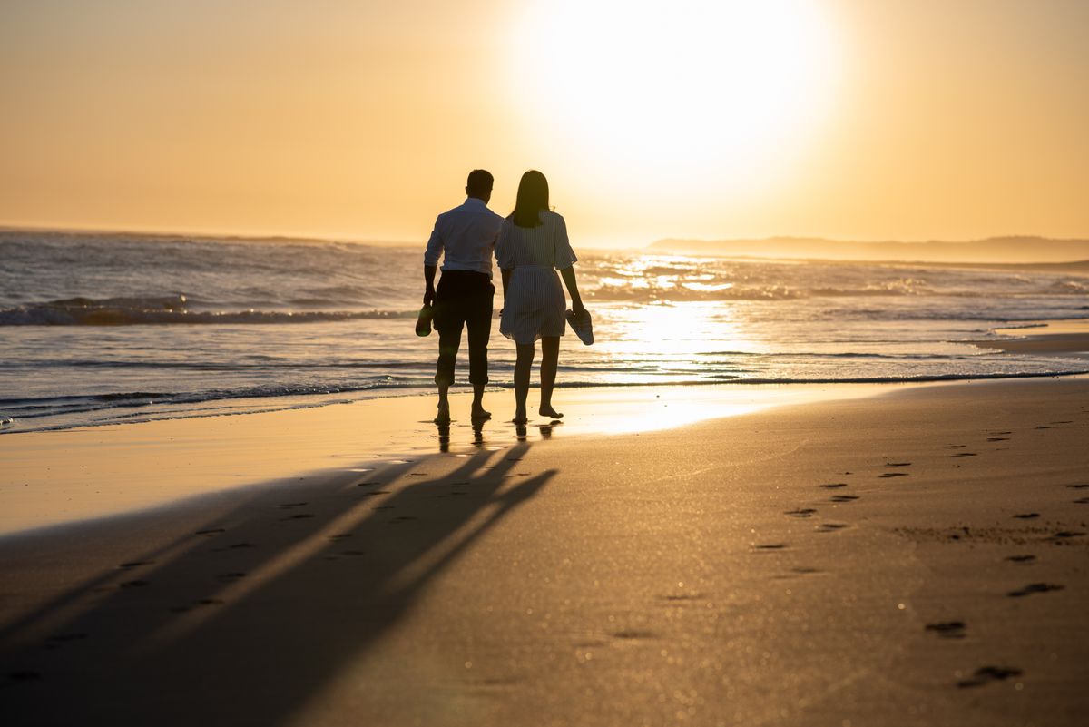 Pareja caminando de la mano por la playa al atardecer
