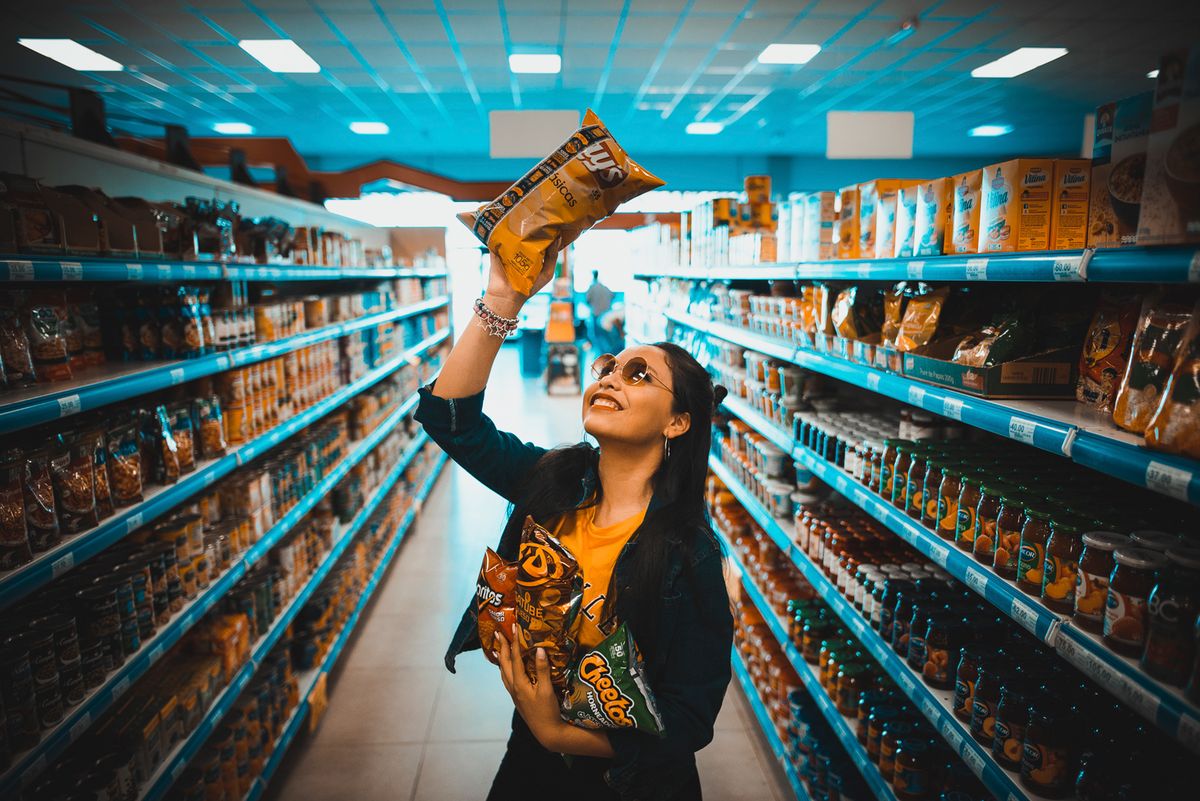 A woman holding two bags of chips in a supermarket aisle