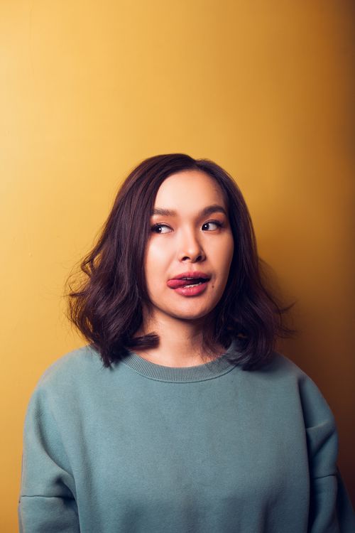 Free Young Asian beautiful woman in oversized sweater licking lips with tongue out looking away while on orange background Stock Photo