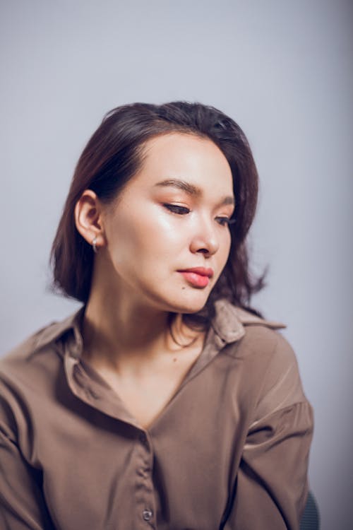 Thoughtful woman with makeup in light brown blouse