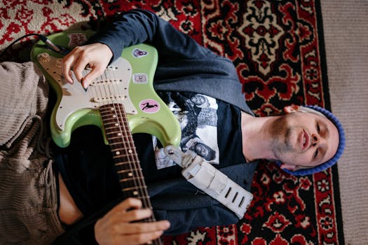 A man lies on a patterned carpet, playing an electric guitar in a cozy home environment.